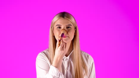 Caucasian-woman-applies-rouge-on-nose-and-cheeks,-makeup,-purple-background