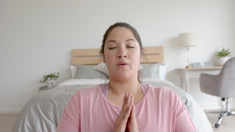 plus size biracial woman sitting on floor practicing yoga meditation and deep breathing, slow motion