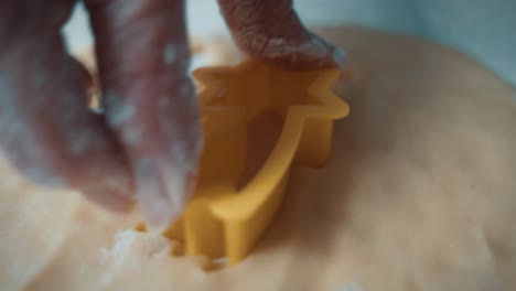 woman's hand cuts the shape of a falling star from fresh, smooth cookie dough on baking sheet