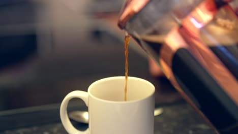 rich black coffee from french press is poured into white ceramic mug