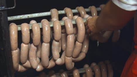 butcher hands places sausages on the bars in the smokehouse