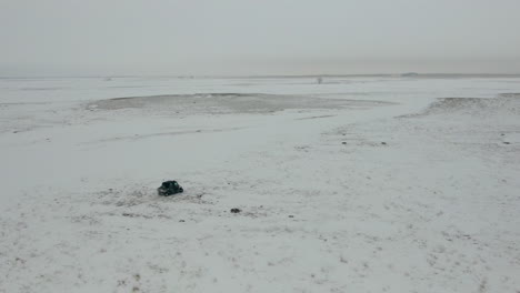 Aerial-of-UTV-side-by-side-driving-across-snow-covered-plain-in-winter,-4K