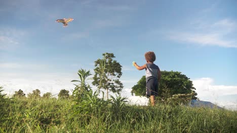 slow motion panning shot from down low behind a young boy flying a kite in africa