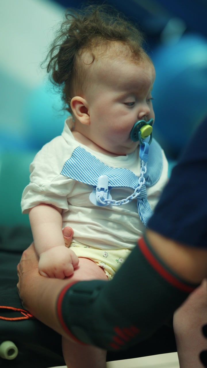 Un bambino dorme profondamente, tenuto in braccio da un genitore. Il piccolo riposa con un ciuccio, trovando conforto e pace.
