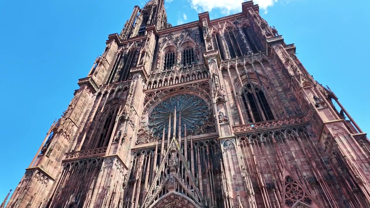 Vista en contrapicado de la ornamentada fachada gótica de piedra de la Catedral de Estrasburgo elevándose hacia el cielo azul.