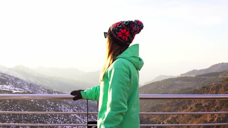 Frau-In-Einer-Grünen-Jacke-Und-Einem-Hut,-Die-An-Einem-Sonnigen-Tag-In-Einer-Verschneiten-Landschaft-In-Die-Kamera-Schaut