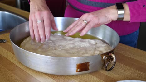 manos esparciendo masa de focaccia en una sartén de metal - horneado casero 60fps