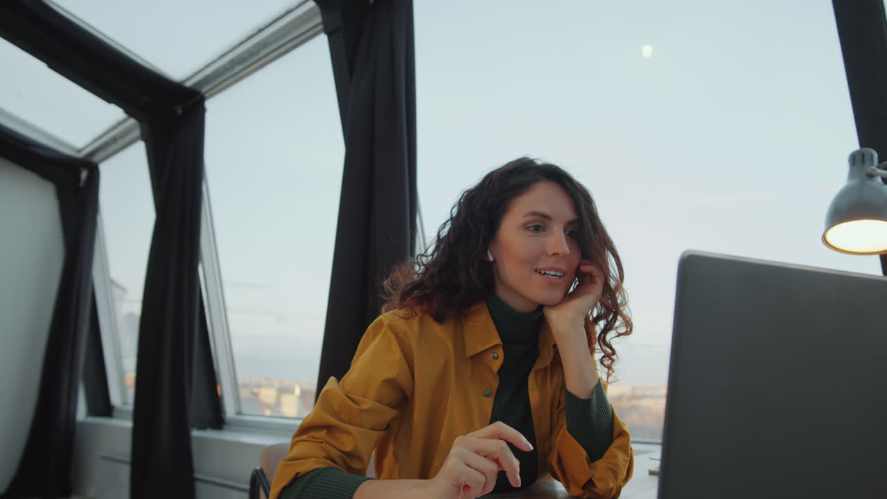 Donna d'affari in videochiamata sul portatile in ufficio panoramico