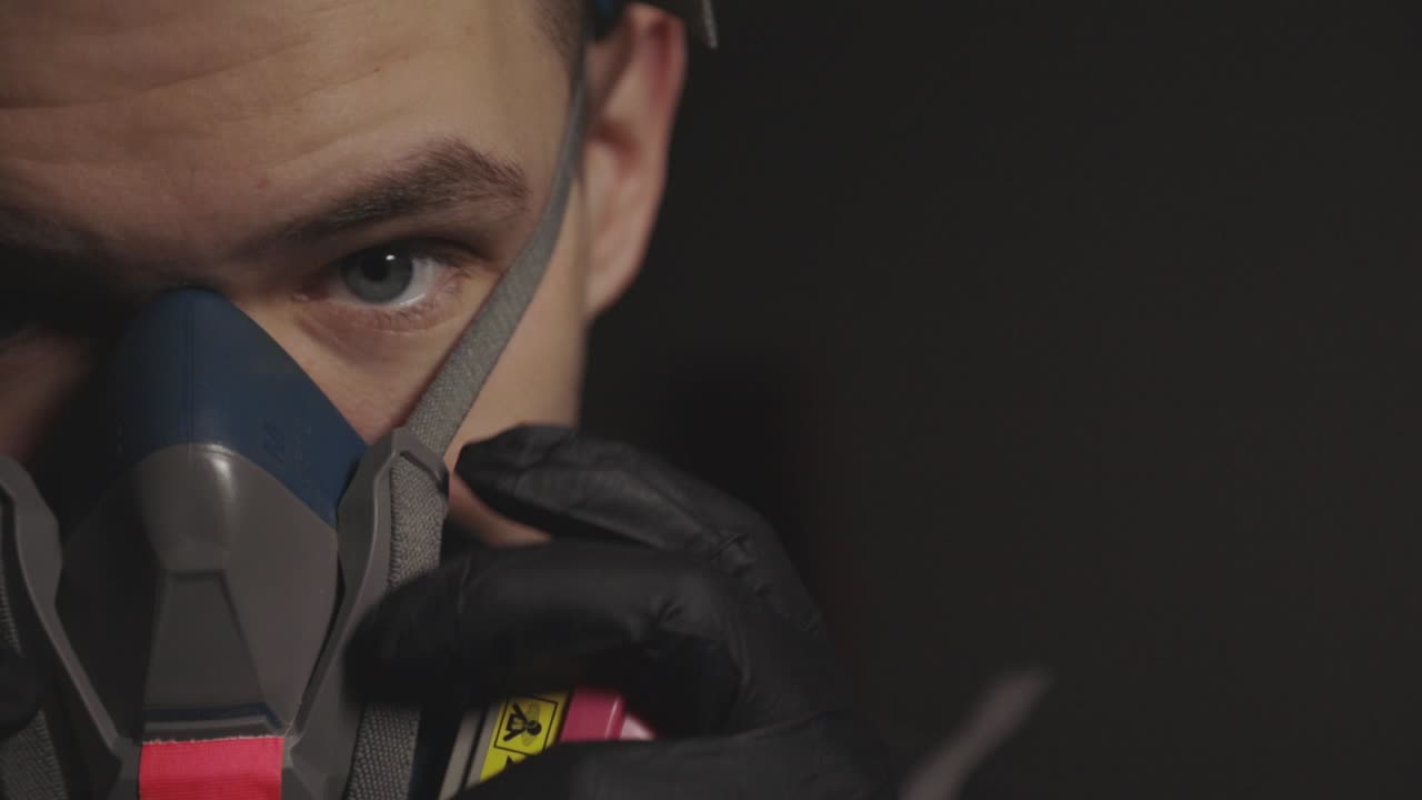 A Man Removing The Respirator That Covers Half Of His Face Using His Black Gloved Hands. -close up shot
