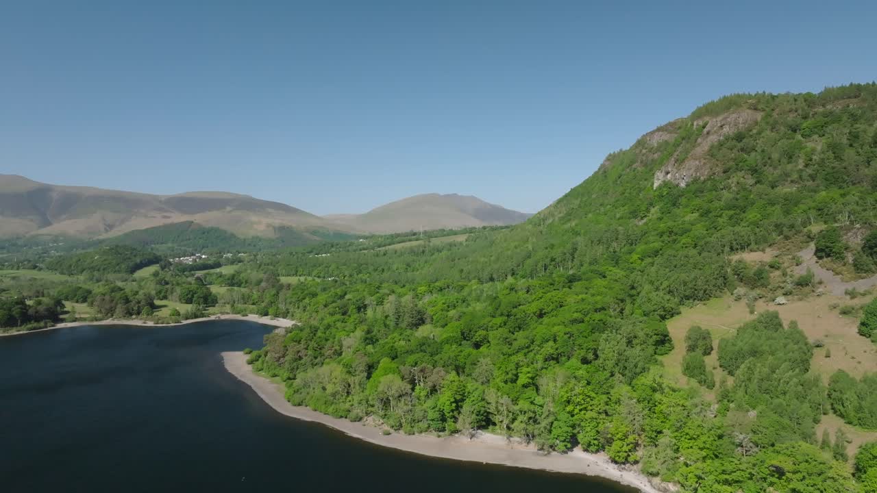 Rising above tree lined Cumbrian lake with views to distant mountains. Derwentwater, Lake District, Cumbria, UK.
