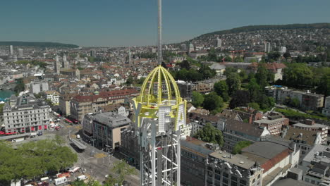 Tiro-Aéreo-Cercano-De-Un-Dron-Orbitando-Alrededor-Y-Levantándose-De-La-Torre-De-Caída-Libre-Del-Parque-De-Diversiones-En-Zúrich,-Suiza-Durante-El-Zürichfest