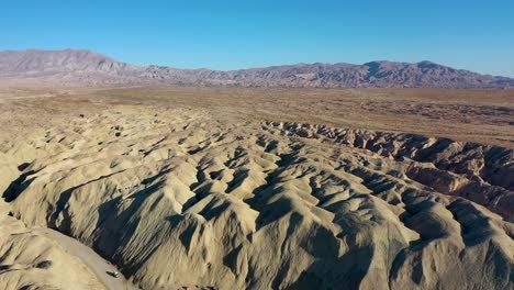 aerial landscape drone flying over hilly arroyo tapiado mud caves towards mountains on hot, dry, sunny day with blue skies