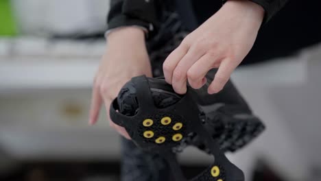 female hands putting ice spikes on shoe during winter, slow motion closeup