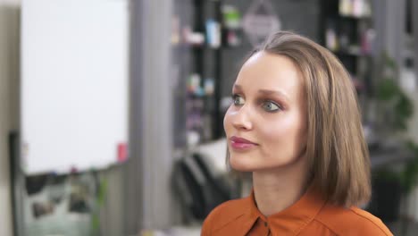 A-blonde-is-sitting-on-the-chair-and-a-make-up-artist-is-finishing-her-visage-with-a-face-spray.-Her-make-up-is-already-finished