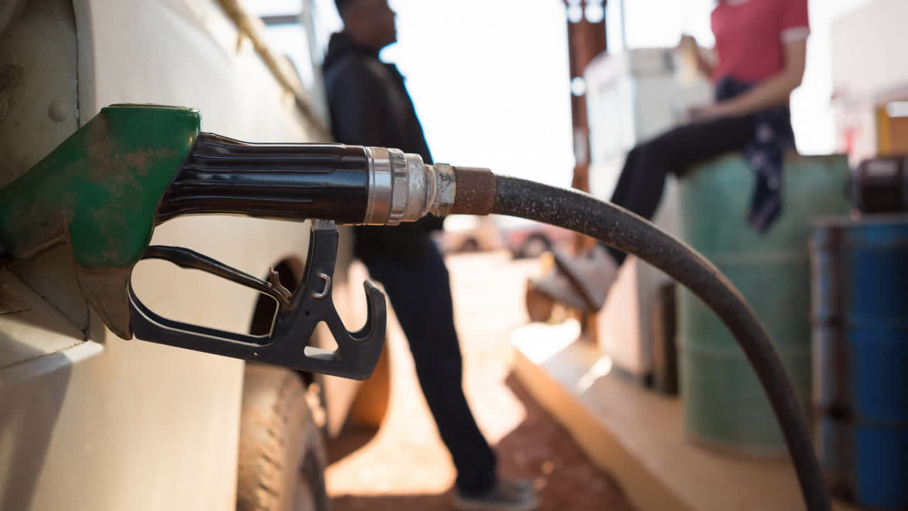 다양한 남성과 여성이 주유소에서 연료  ⁇ 프를 사용하여 트럭을 채우고 있습니다.