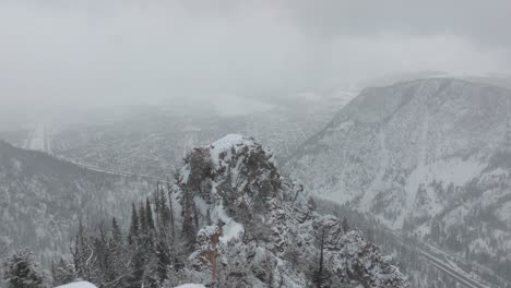 Drone flying past the peak of mountain in snow storm revealing town of Frisco in Colorado, USA.
