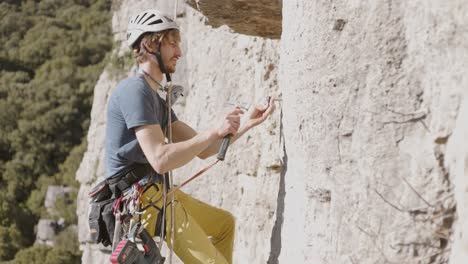 escalada en roca - escalador en arnés de seguridad colgando en el acantilado y martillando el clavo de expansión en el acantilado de la montaña