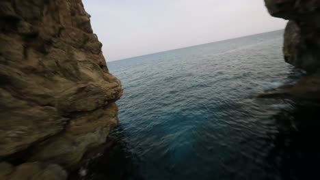 FPV-drone-shot-of-steep-cliffs-and-natural-stone-bridge-along-the-seaside-in-Cala-Varques,-Mallorca,-Spain-during-evening-time