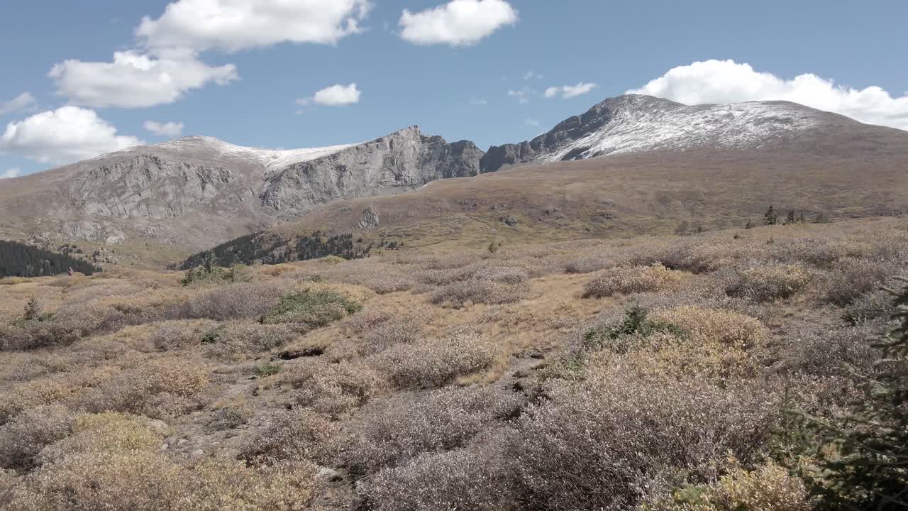 Aerial view over a remote mountain hillside in the fall with Mount Blue Sky and Bierstadt in the distance with snow towards the peak. Filmed near Guanella Pass, Colorado. Dolly and panning movement.