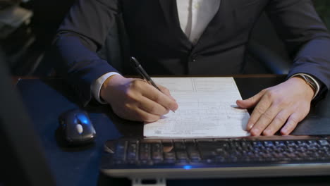 a man in a suit at a desk, near a computer, studying a form to compile