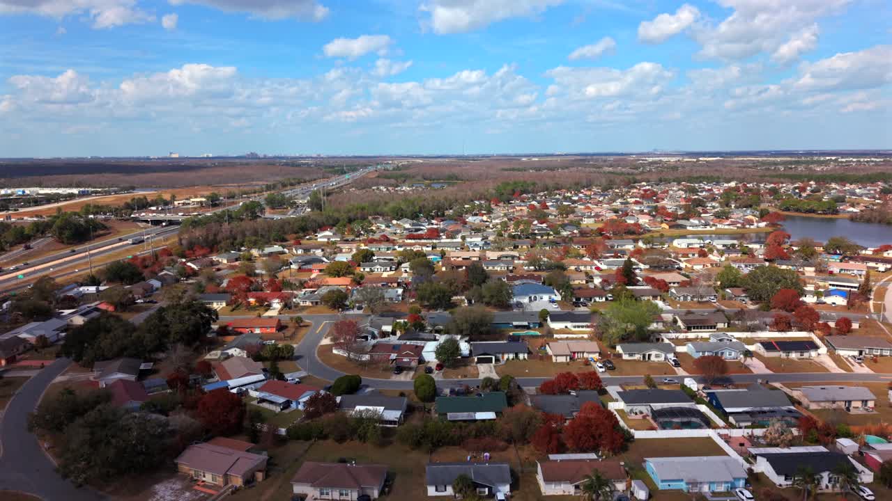 Uma vista aérea de um bairro residencial em Kissimmee, Flórida, em um dia ensolarado com céu azul e nuvens brancas. A câmera do drone se aproxima sobre um lago e casas.