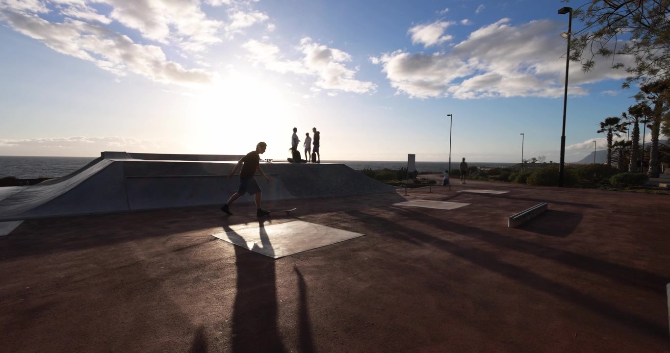 Silhouette di uno skateboarder che fa skateboard al tramonto in uno skatepark fronte oceano