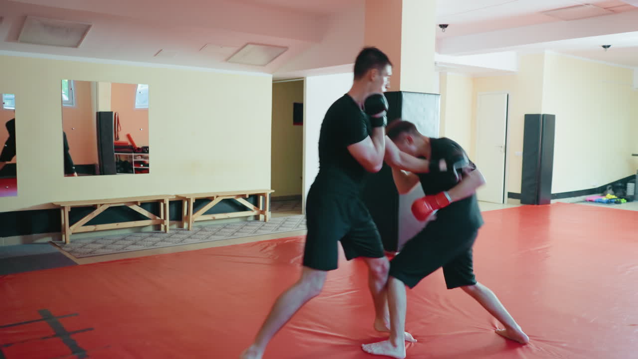 Karate practitioners sparring on red mat in dojo, wearing protective gloves, engaged in combat training, practicing strikes, blocks, movement,martial arts spirit, athletic preparation, intense focus