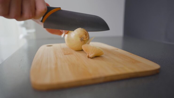 Uomo che affetta una cipolla marrone con un coltello da cucina