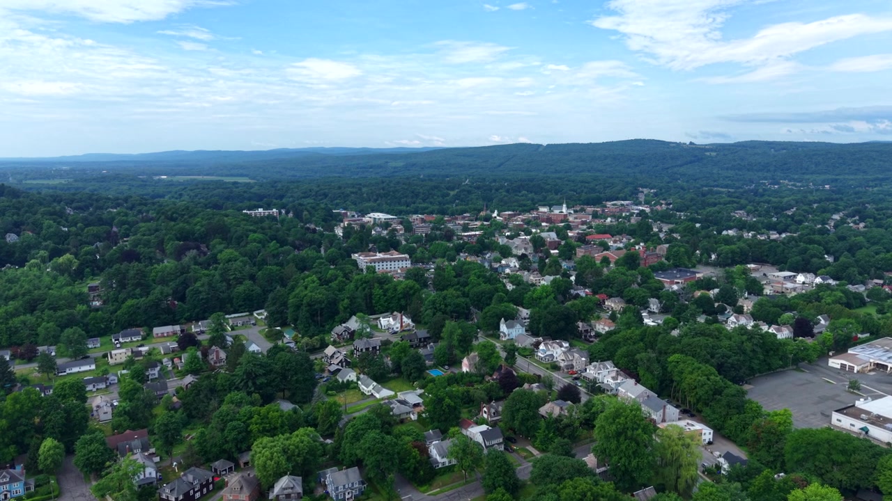Træbeklædte kvarterer spredt ud over Greenfield, Massachusetts nær Poets Seat Tower-området, skovklædte bakker omgiver historisk New England-by under varm sommerhimmel. Bredt dronebillede