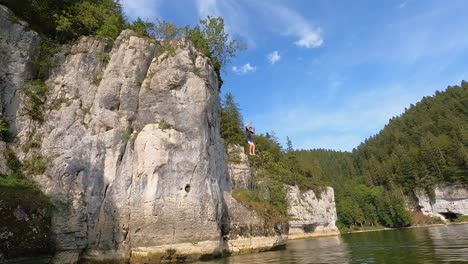 a young jumps from a high rocky cliff into the water of the doubs river, switzerland