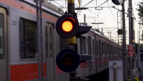 Close-up-of-train-crossing-lights-with-trains-passing-by-in-either-direction,-Tokyo,-Japan