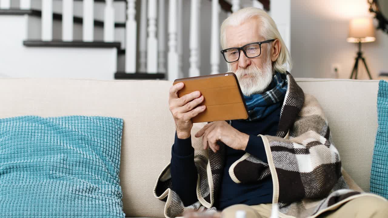 retrato de un hombre enfermo sentado en una habitación acogedora y tocando en la tableta