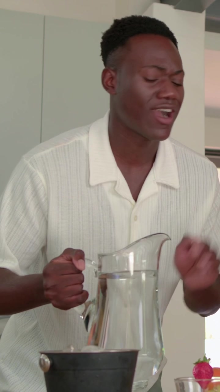 Video verticale: Uomo in camicia in cucina che mescola fuori campo in un secchio nero e versa da una brocca per le bevande