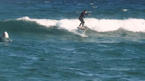 A-surfer-catches-a-wave-using-a-highly-entertaining-foil-system-at-Guincho-Beach-in-Cascais,-combining-thrill-with-innovation-in-the-world-of-surfing