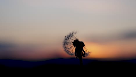 a person blows in a dandelions blowball which is in front of a beautiful sunset