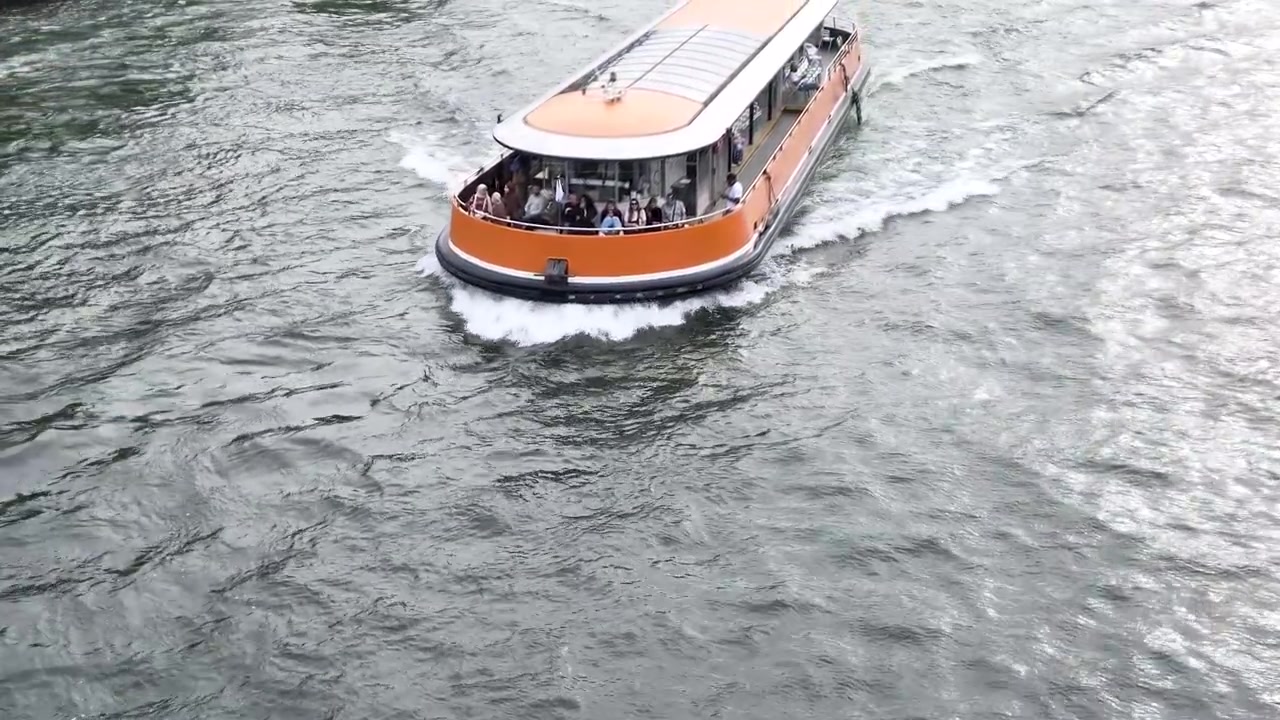 Tomada aérea de um barco turístico laranja navegando pelo Rio Sena em Paris.