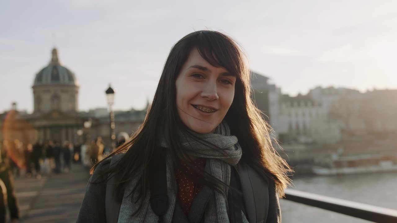 Portrait of happy beautiful young elegant woman smiling with brackets on camera at sunset Paris square slow motion.