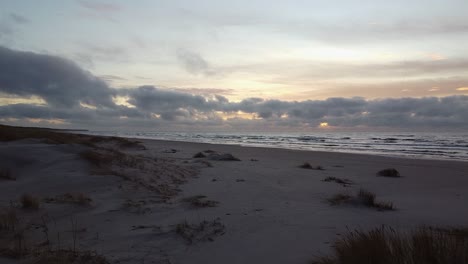 Aerial-drone-flyover-at-Perkone-sandy-beach-Baltic-sea-coastline-after-the-sunset,-no-people,-autumn,-spring,-moving-forward-over-the-dunes