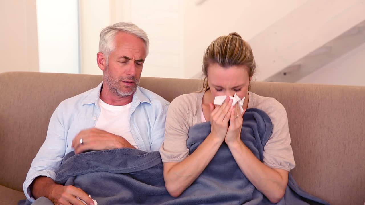 Sick couple sitting on the couch under a blanket