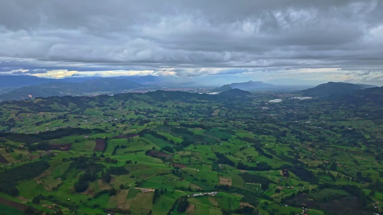Drone pulls back over Zipaquira farmland with cloudy skies and layered hills