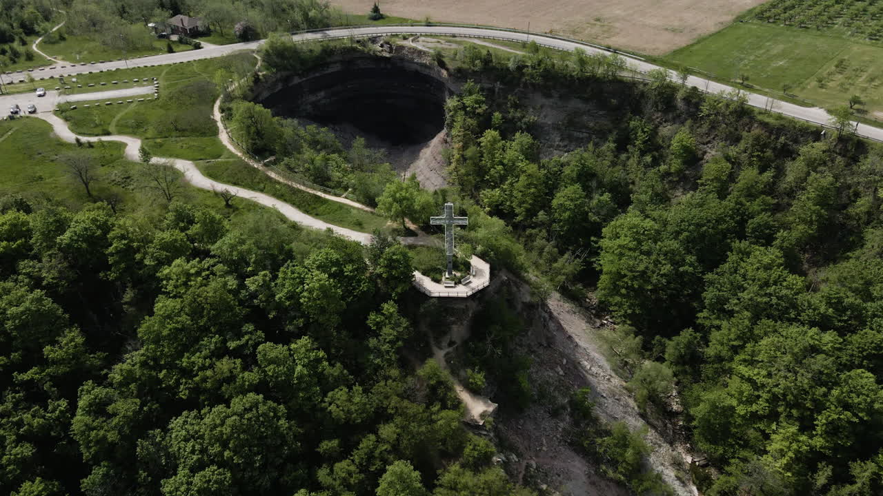 Aerial tilt down flight towards cross memorial standing on hill of Devils Punch Bowl, Ontario,Canada. Beautiful sunny day surrounded by farm fields.