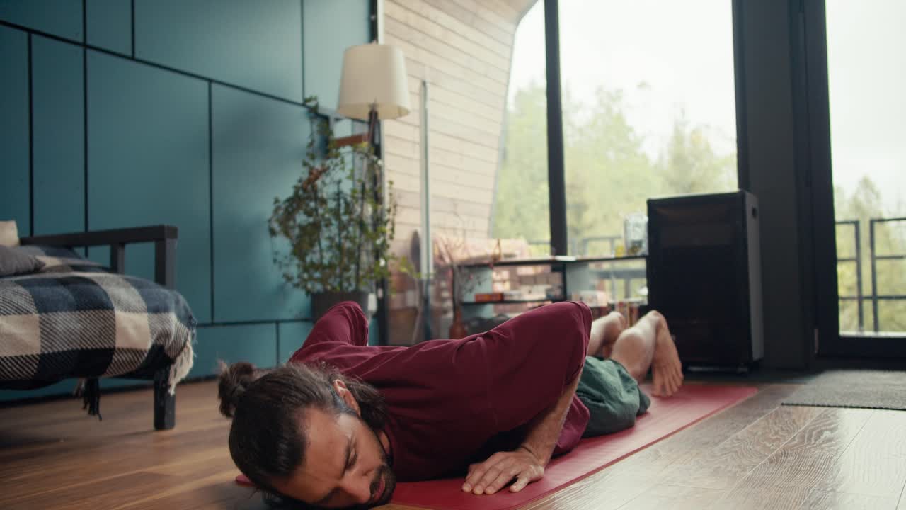 un tipo moreno feliz con una camiseta roja está cansado de hacer flexiones y acostarse en una alfombra roja para descansar. clases de fitness en casa
