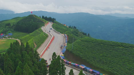 The-drone-takes-a-smooth-flight-over-a-popular-tourist-destination,-the-lush-green-tea-gardens-of-Kanyam-in-Ilam,-Nepal,-showcasing-a-scenic-highway-winding-through-the-verdant-landscape