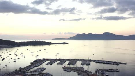 AERIAL:-Ocean-with-Sailboats-and-Tropical-Island-with-Mountains-in-Background-at-Sunrise-Vacation,-Travel,-Sunset