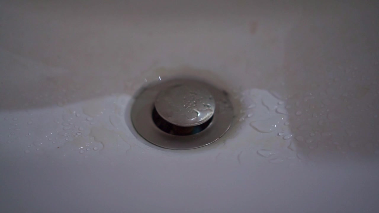 Water droplets dripping on metal sink drain, close up view, wet surface, kitchen or bathroom plumbing, hygiene concept footage.