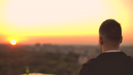 view from the back a man walks on the roof at sunset and drinks beer looking at the beautiful view of the city.