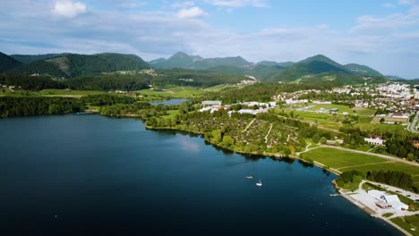 Aerial-landscape-shot-of-coast-of-lake-velenjsko-with-town-and-hills-in-the-background-slovenia-europe