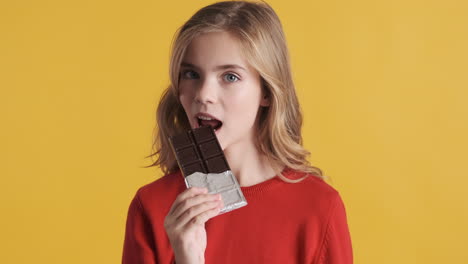 teenage caucasian girl eating chocolate bar in front of the camera.