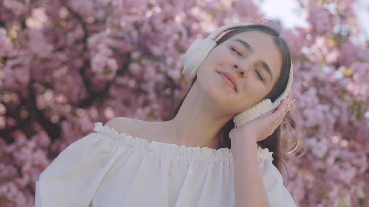 Teenage girl enjoying music in a cherry blossom garden