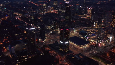 Aerial-shot-of-downtown-at-night.-Tilt-up-reveal-of-cityscape.-Traffic-on-roads-in-city.-Warsaw,-Poland